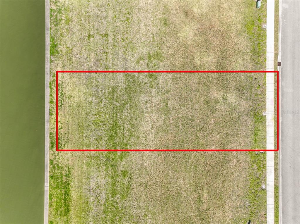 An aerial view shows a rectangular vacant lot situated between a road and a canal — 268 HARBOR VILLAGE POINT N, PALM COAST, FL