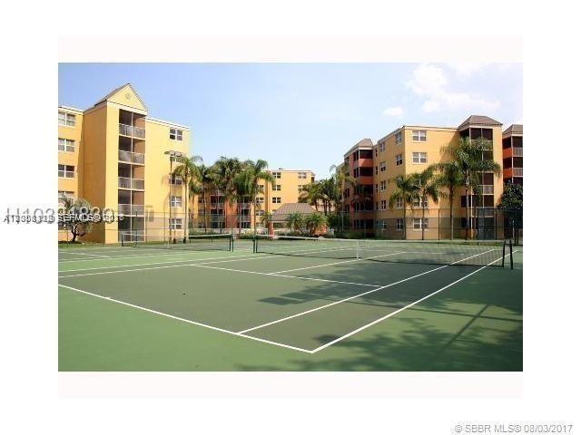 A tennis court sits in front of multi-story yellow apartment buildings with palm trees — 8363 Lake Dr # 102, Doral FL 33166, DORAL, FL