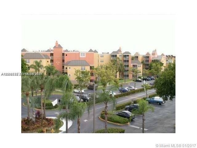An exterior view of a multi-story apartment complex with a parking lot and palm trees — 8363 Lake Dr # 102, Doral FL 33166, DORAL, FL