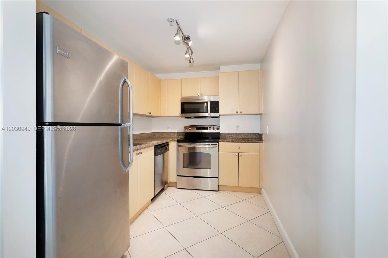 A galley kitchen features light wood cabinets, stainless steel appliances, and beige tile flooring — 2280 SW 32nd Ave # 605, Miami FL 33145, MIAMI, FL