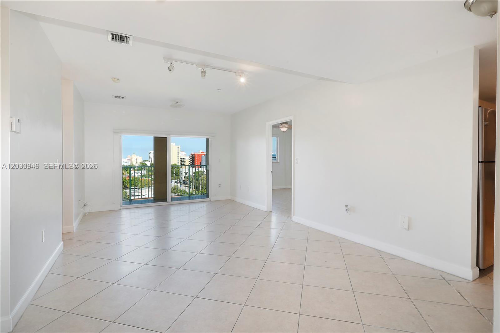An empty living room features white walls, tile flooring, track lighting, and a sliding glass door — 2280 SW 32nd Ave # 605, Miami FL 33145, MIAMI, FL