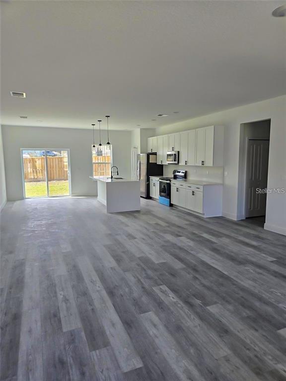An open-concept kitchen and living area features white cabinets, stainless steel appliances, and gray flooring — 15092 SW 52ND COURT, OCALA, FL