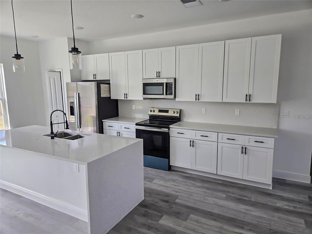 A modern kitchen features white cabinetry, quartz countertops, stainless steel appliances, and a central island — 15092 SW 52ND COURT, OCALA, FL
