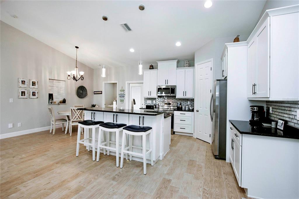 A modern kitchen features white cabinets, black countertops, a center island with stools, and wood-look flooring — 4446 BAYANO STREET, NORTH PORT, FL