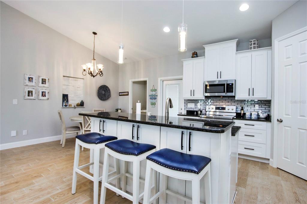 A kitchen features white cabinetry, a dark granite island with blue stools, and light flooring — 4446 BAYANO STREET, NORTH PORT, FL