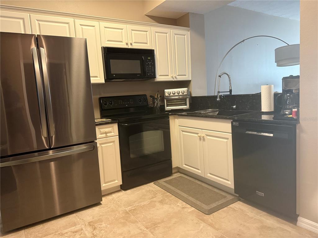 A kitchen with white cabinets, stainless steel appliances, a black dishwasher, and dark countertops — 3506 54TH DRIVE W UNIT 203, BRADENTON, FL