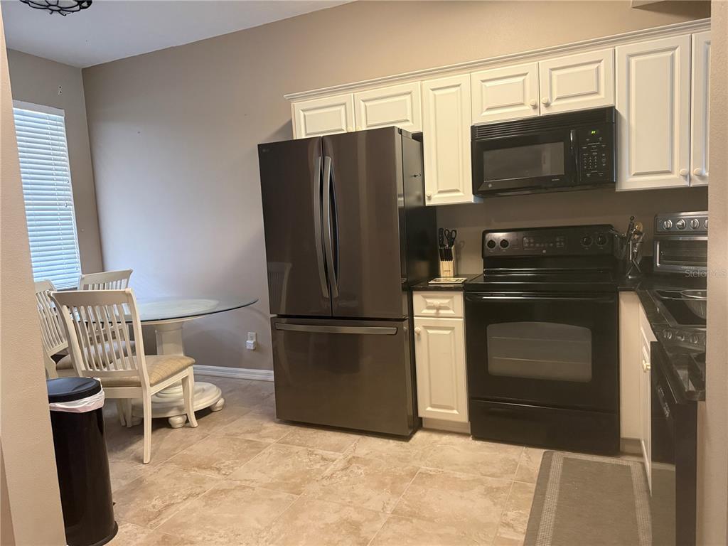 A kitchen features white cabinets, a black stove, a stainless steel refrigerator, and a dining area — 3506 54TH DRIVE W UNIT 203, BRADENTON, FL