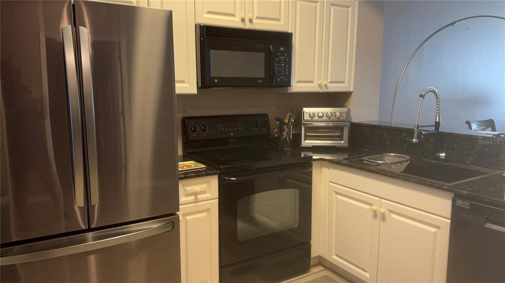 A kitchen features white cabinets, black countertops, stainless steel appliances, and a black range — 3506 54TH DRIVE W UNIT 203, BRADENTON, FL