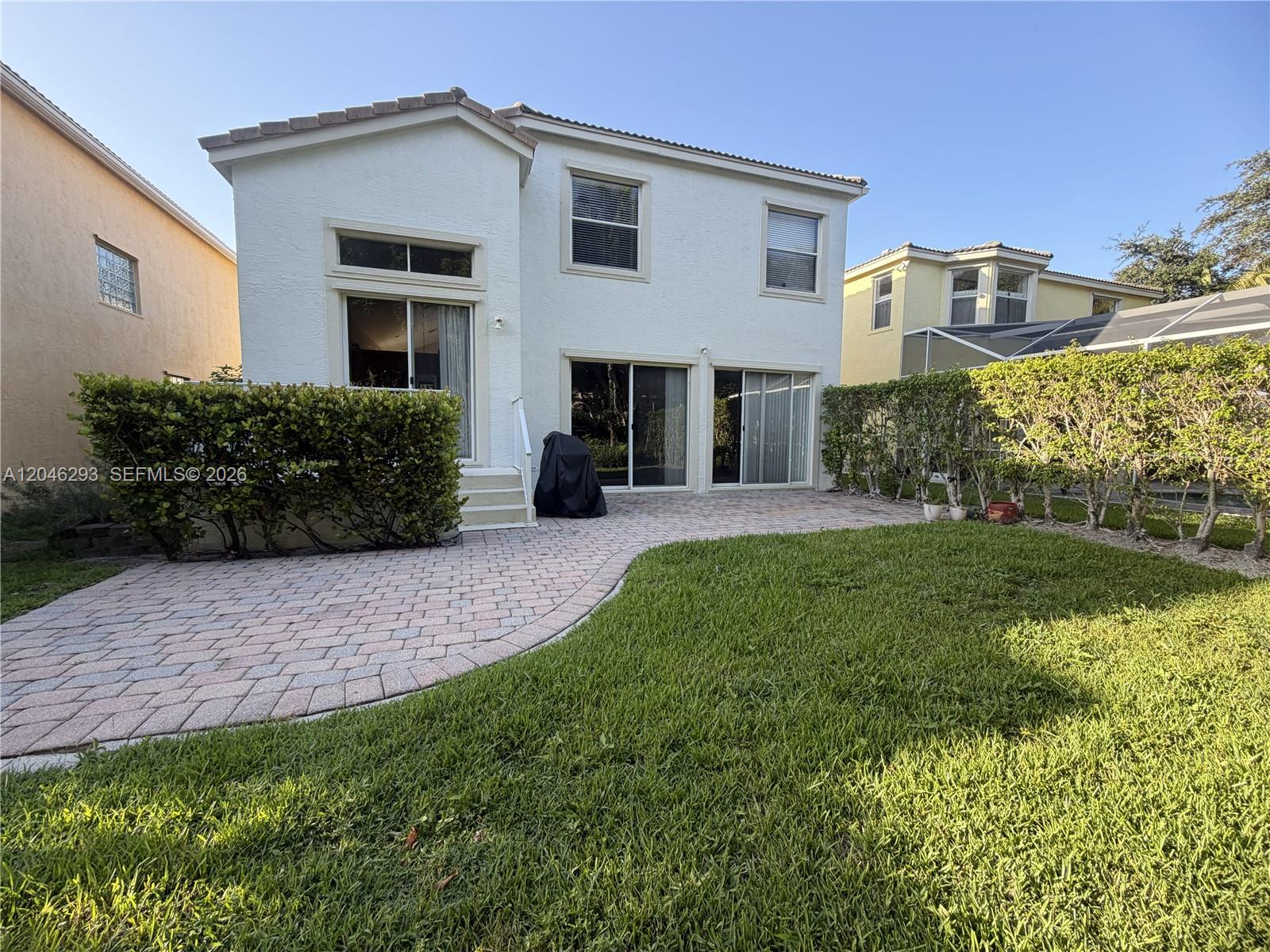 The exterior of a two-story house features a paved patio, green lawn, and privacy hedges — 9640 Wyeth Ct, Wellington FL 33414, WELLINGTON, FL