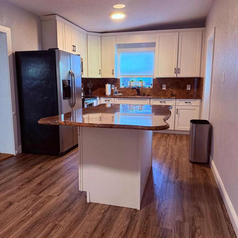 A kitchen features white cabinets, granite countertops, a central island, and wood-look flooring — 2940 LAKE MARGARET DRIVE, ORLANDO, FL