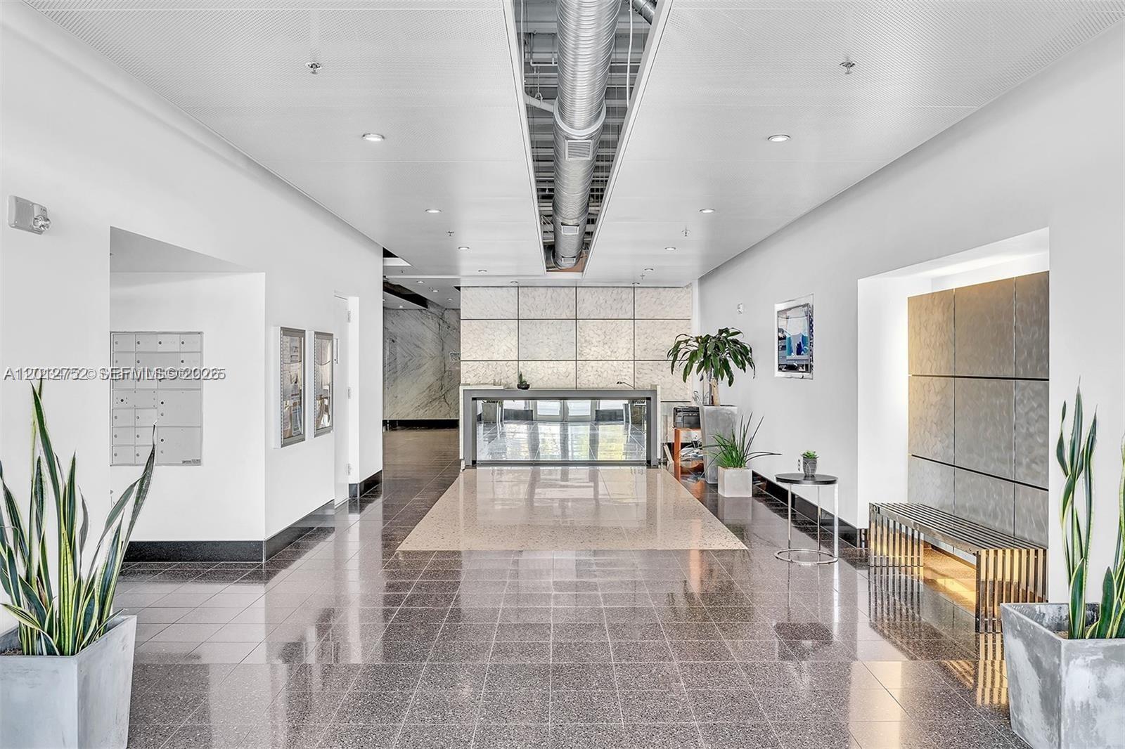 A modern building lobby features a reception desk, tiled floors, and decorative potted plants — 8101 Biscayne Blvd # 410, Miami FL 33138, MIAMI, FL