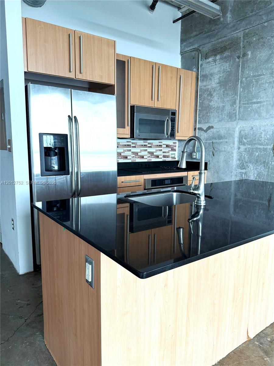 A kitchen features light wood cabinets, black countertops, stainless steel appliances, and an exposed concrete wall — 8101 Biscayne Blvd # 410, Miami FL 33138, MIAMI, FL