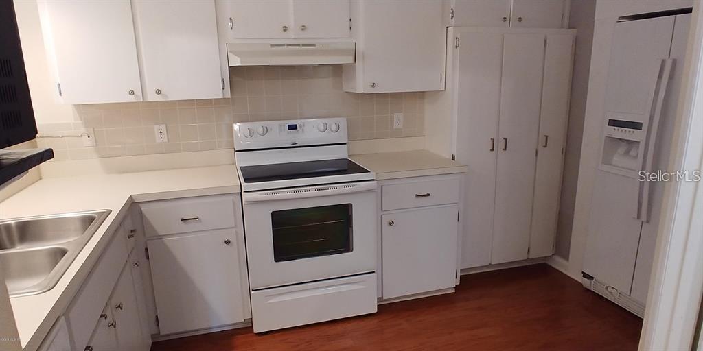 A kitchen features white cabinets, white appliances, a double sink, and wood-look flooring — 2028 NW 50TH AVENUE, OCALA, FL