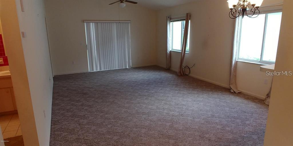 An empty living room features beige carpeting, a ceiling fan, and sliding glass doors — 2028 NW 50TH AVENUE, OCALA, FL
