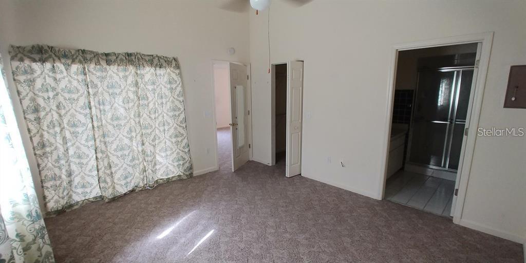 A bedroom with beige carpet, patterned curtains, a closet, and an attached bathroom — 2028 NW 50TH AVENUE, OCALA, FL
