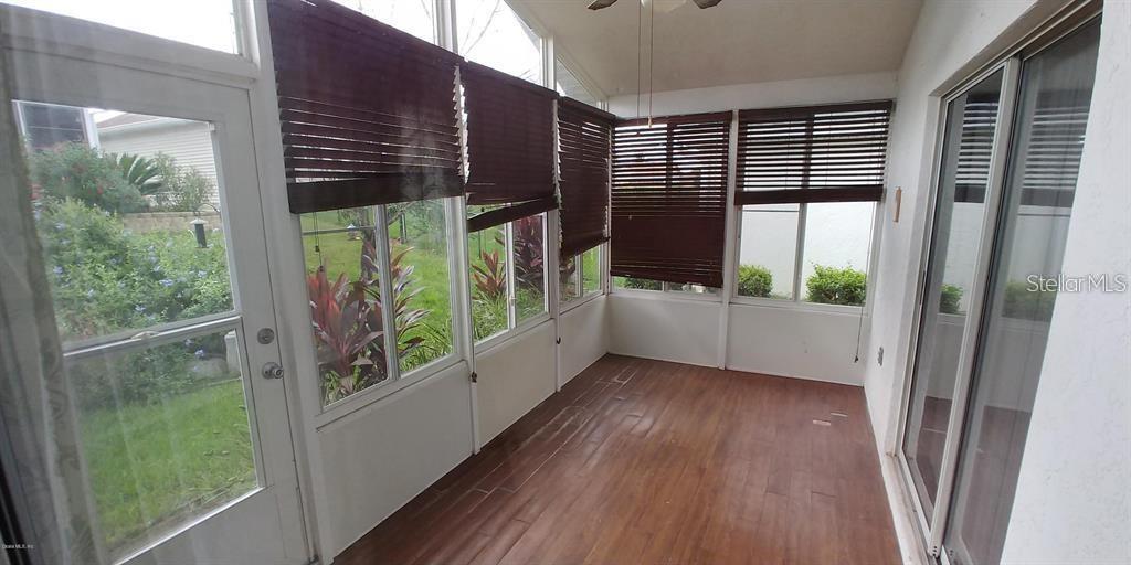 A sunroom features wood-look flooring, dark window blinds, and a glass door leading outside — 2028 NW 50TH AVENUE, OCALA, FL