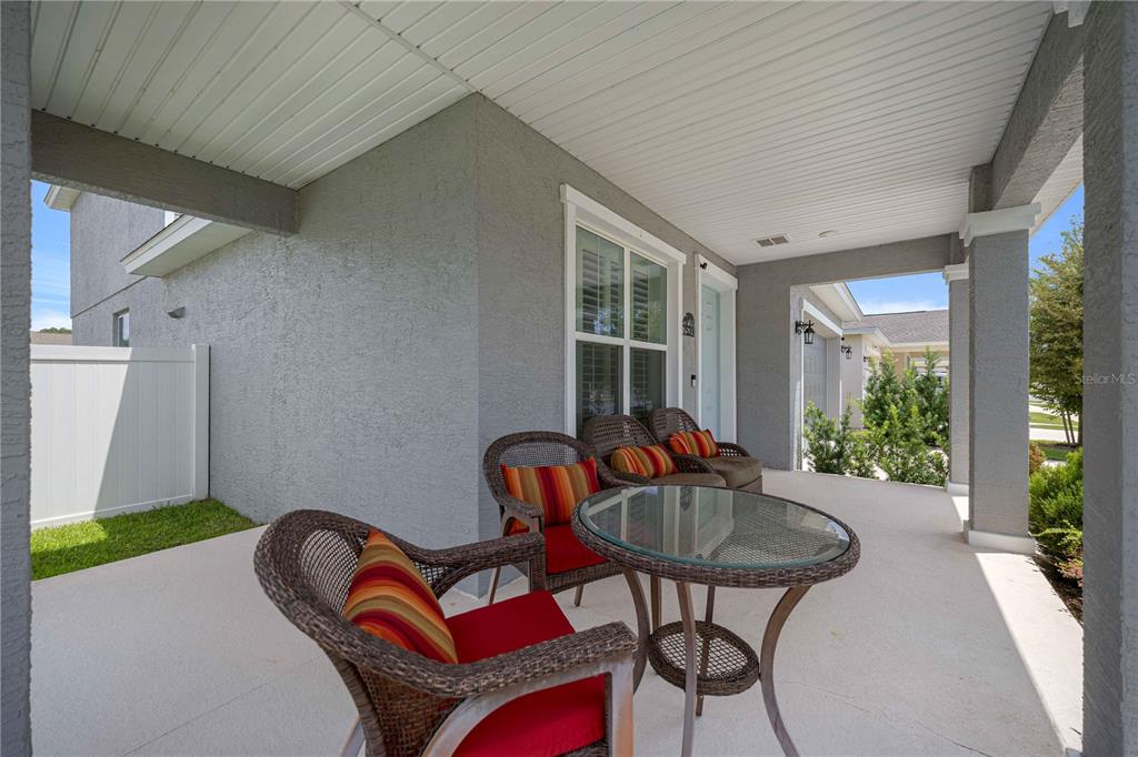 A covered concrete patio features wicker furniture with red striped cushions and a glass table — 7539 SW 64TH STREET ROAD, OCALA, FL