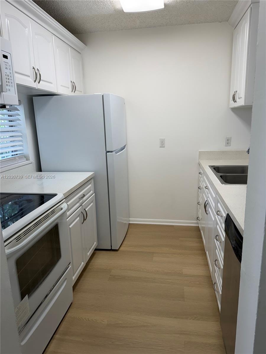 A galley kitchen features white cabinets, white appliances, a stainless steel dishwasher, and light flooring — 8560 N Sherman Cir # 404, Miramar FL 33025, MIRAMAR, FL
