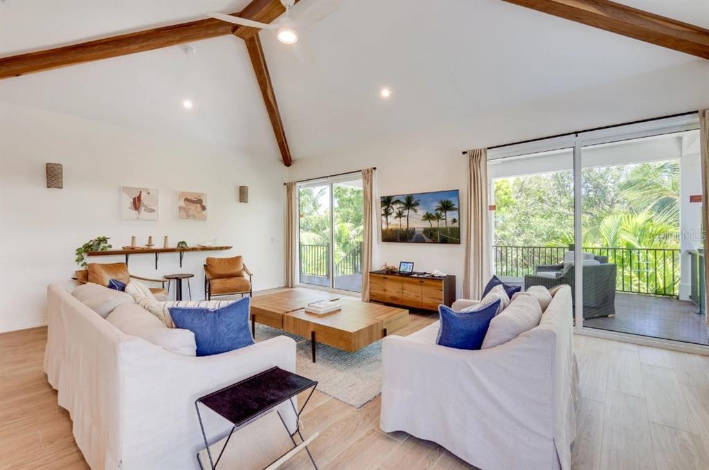 A living room with a vaulted ceiling, exposed beams, white sofas, and sliding glass doors — 9407 GULF DR, ANNA MARIA, FL