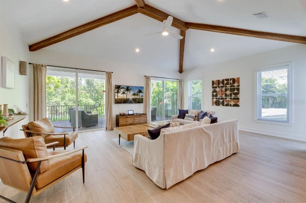A living room features vaulted ceilings with exposed beams, light wood floors, and sliding glass doors — 9407 GULF DR, ANNA MARIA, FL