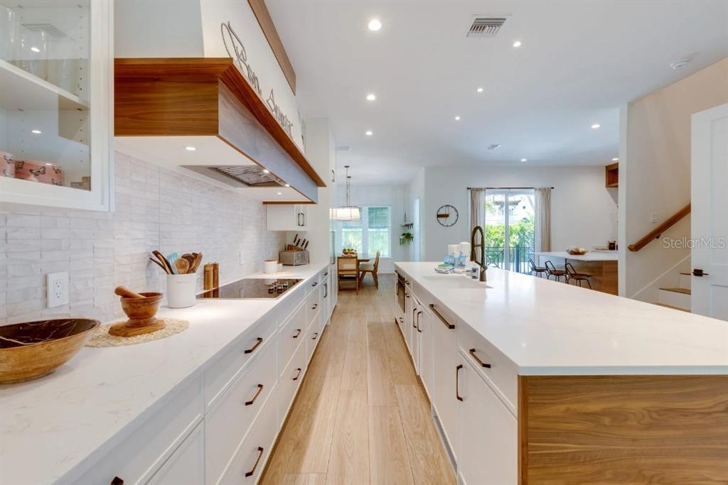 A modern kitchen features white cabinetry, quartz countertops, wood accents, and a large center island — 9407 GULF DR, ANNA MARIA, FL
