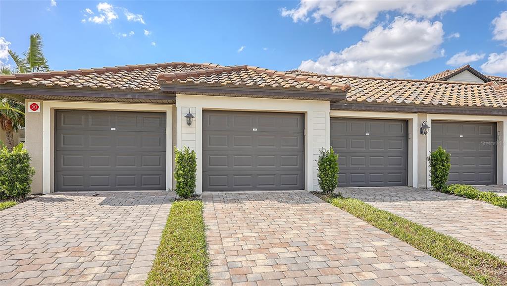A row of three garage doors with a paver driveway under a tiled roof — 5710 PALMER CIRCLE UNIT 201, BRADENTON, FL