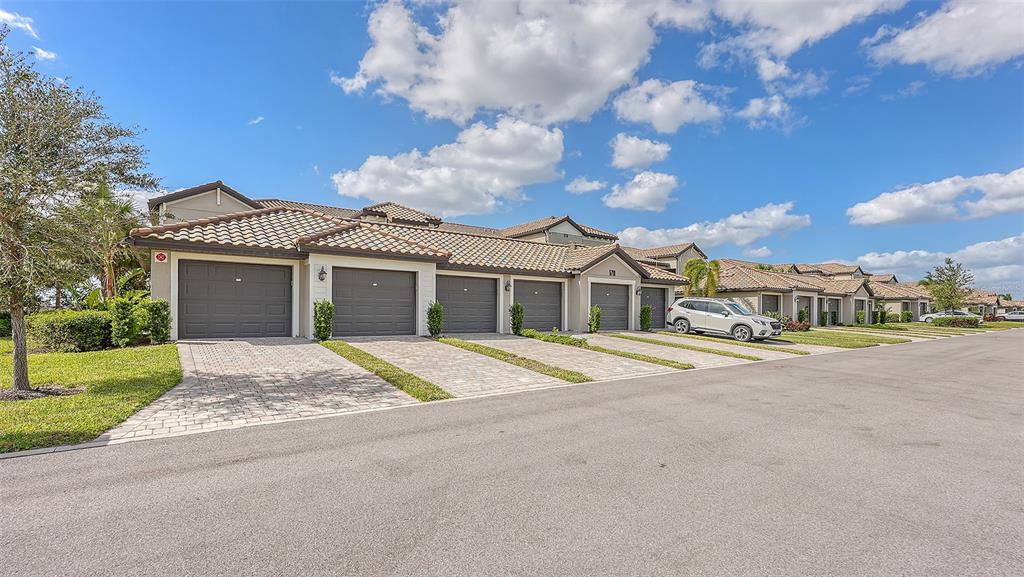 A row of attached townhomes with grey garage doors and tiled roofs under a blue sky — 5710 PALMER CIRCLE UNIT 201, BRADENTON, FL