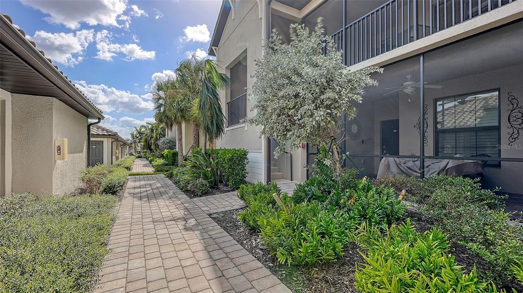 A paved walkway leads between two residential buildings with landscaped gardens and a screened patio — 5710 PALMER CIRCLE UNIT 201, BRADENTON, FL