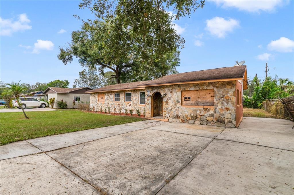 A single-story house with a stone facade and boarded-up windows sits behind a concrete driveway — 6427 SUNSHINE STREET, ORLANDO, FL