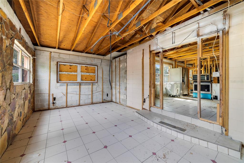 An unfinished room with exposed ceiling rafters, tiled flooring, and a stone wall section — 6427 SUNSHINE STREET, ORLANDO, FL