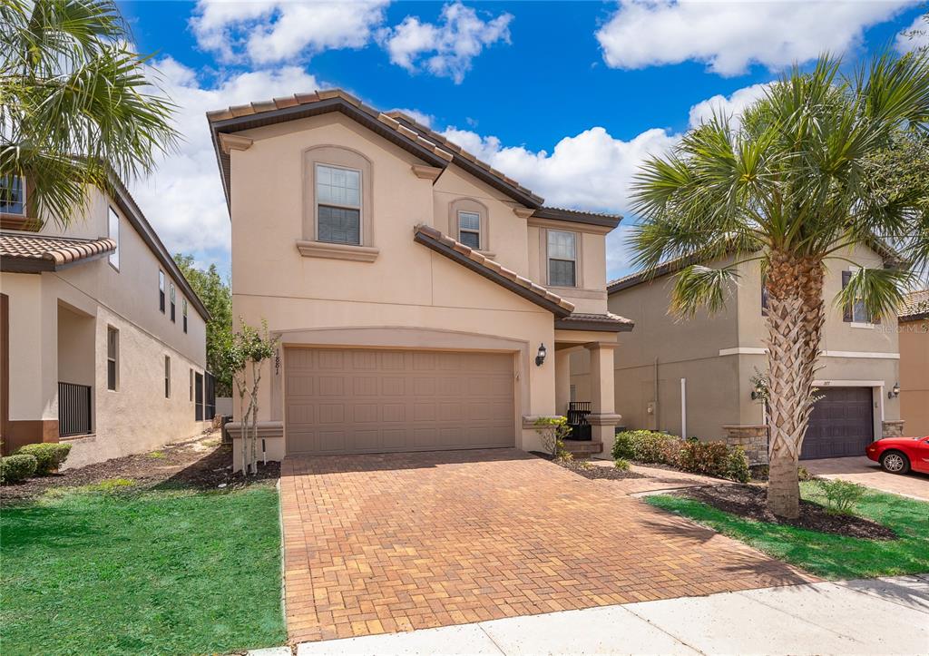 A two-story tan stucco house with a brick paver driveway and a two-car garage — 1881 NICE COURT, KISSIMMEE, FL