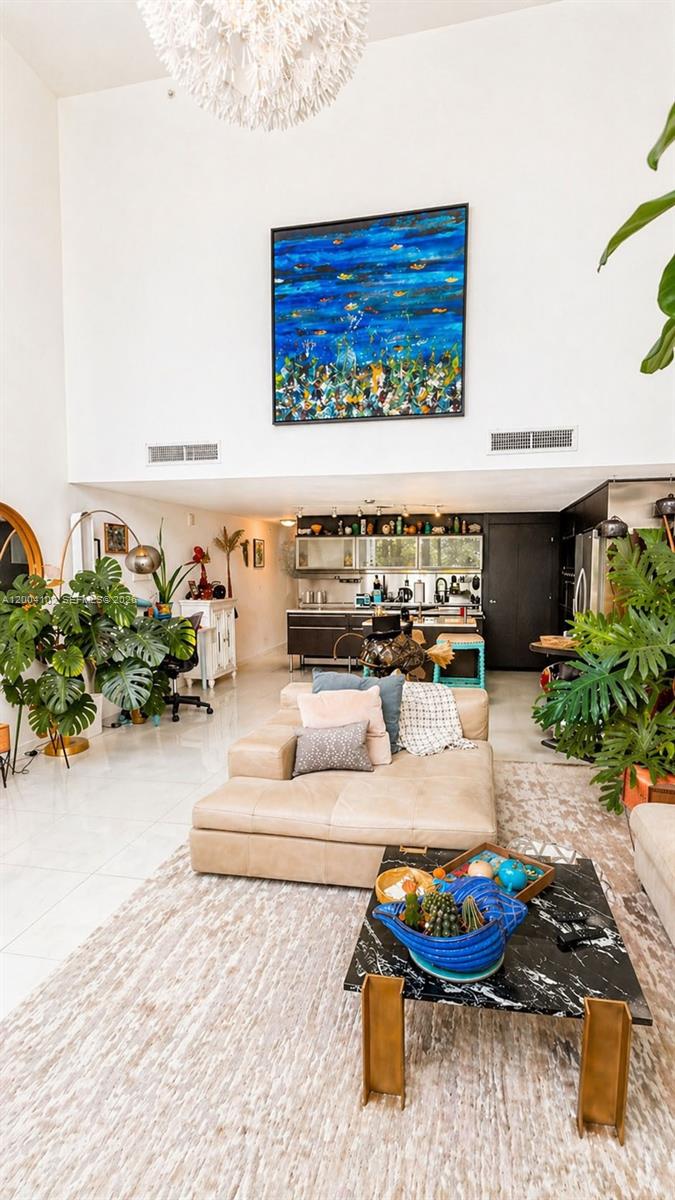 A high-ceilinged living room features a beige sectional sofa, a black marble coffee table, and plants — 6000 Collins Ave # 515, Miami Beach FL 33140, MIAMI BEACH, FL