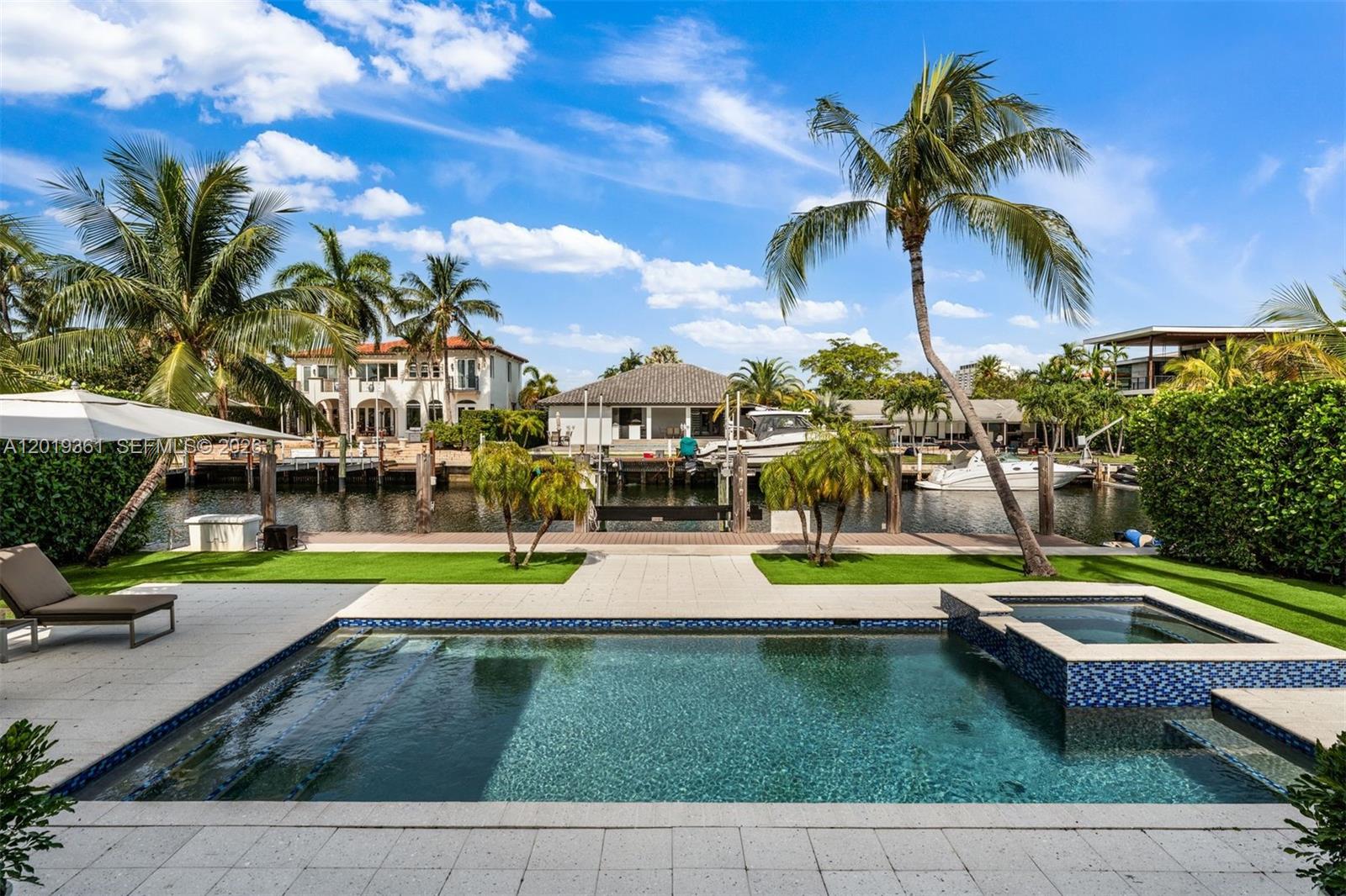 A swimming pool and hot tub overlook a canal with boat docks and palm trees — 13040 N Bayshore Dr, North Miami FL 33181, NORTH MIAMI, FL