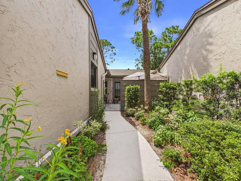 A concrete walkway leads between two stucco buildings toward a gated courtyard with a palm tree — 407 MEADOWOOD BOULEVARD, FERN PARK, FL