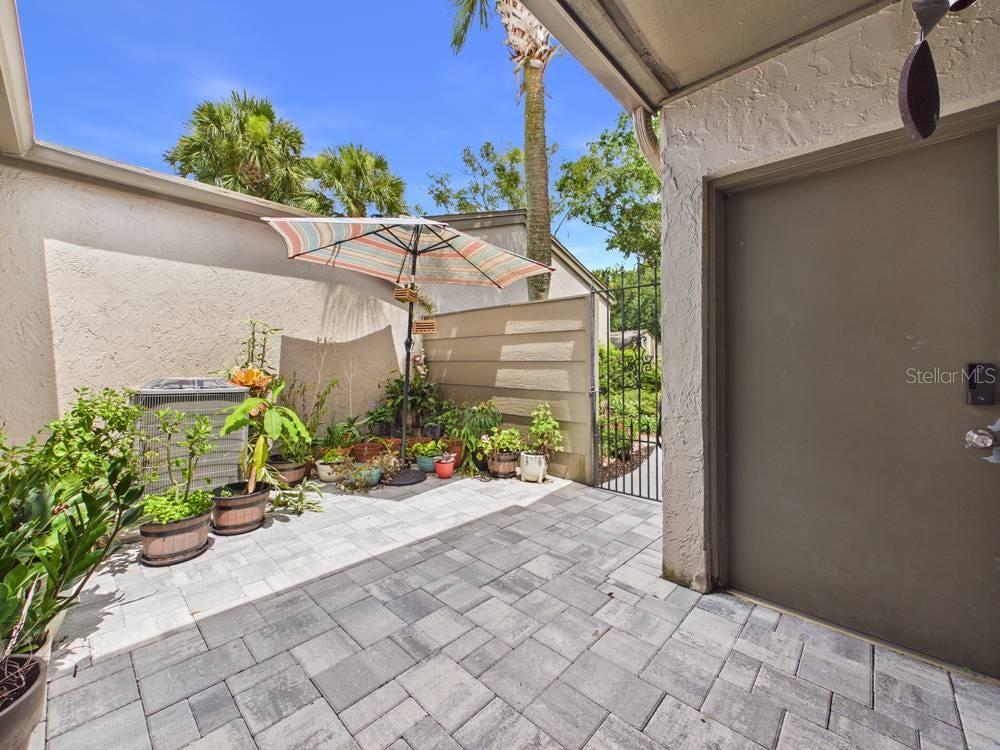 A paved patio features a striped umbrella, potted plants, an air conditioning unit, and a door — 407 MEADOWOOD BOULEVARD, FERN PARK, FL