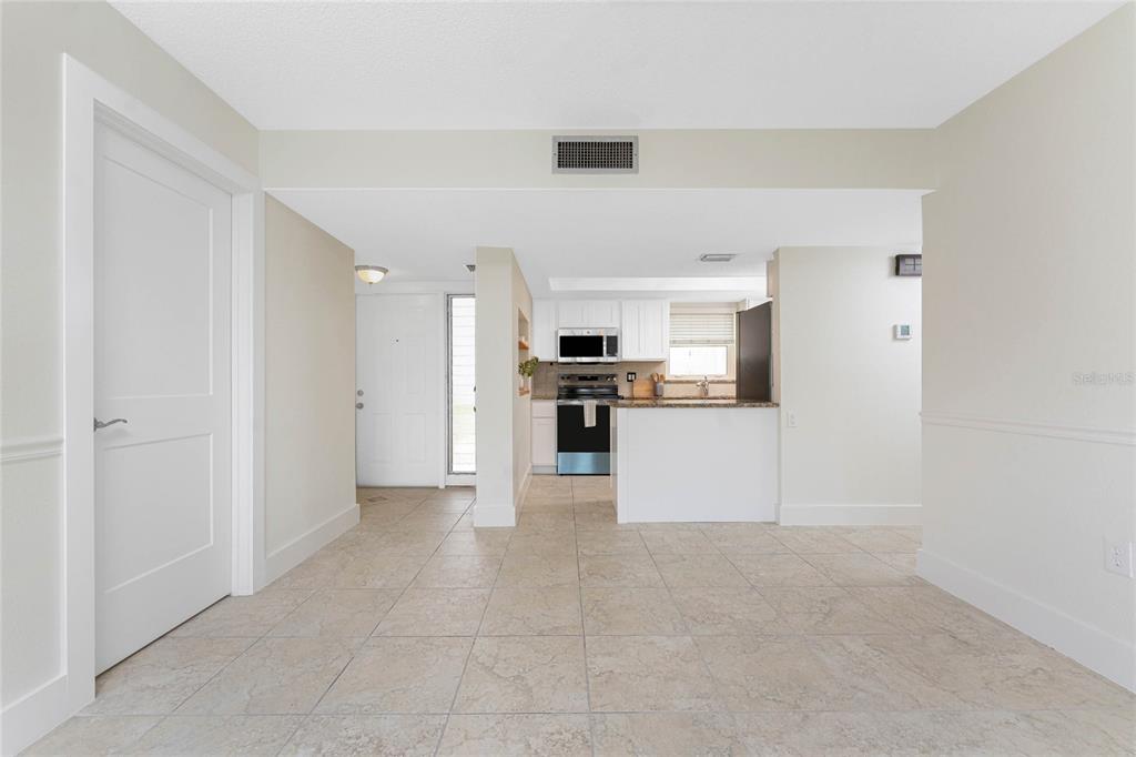 A view of a tiled living area looking toward a kitchen with white cabinets — 1080 BAL HARBOR BOULEVARD UNIT 1A, PUNTA GORDA, FL
