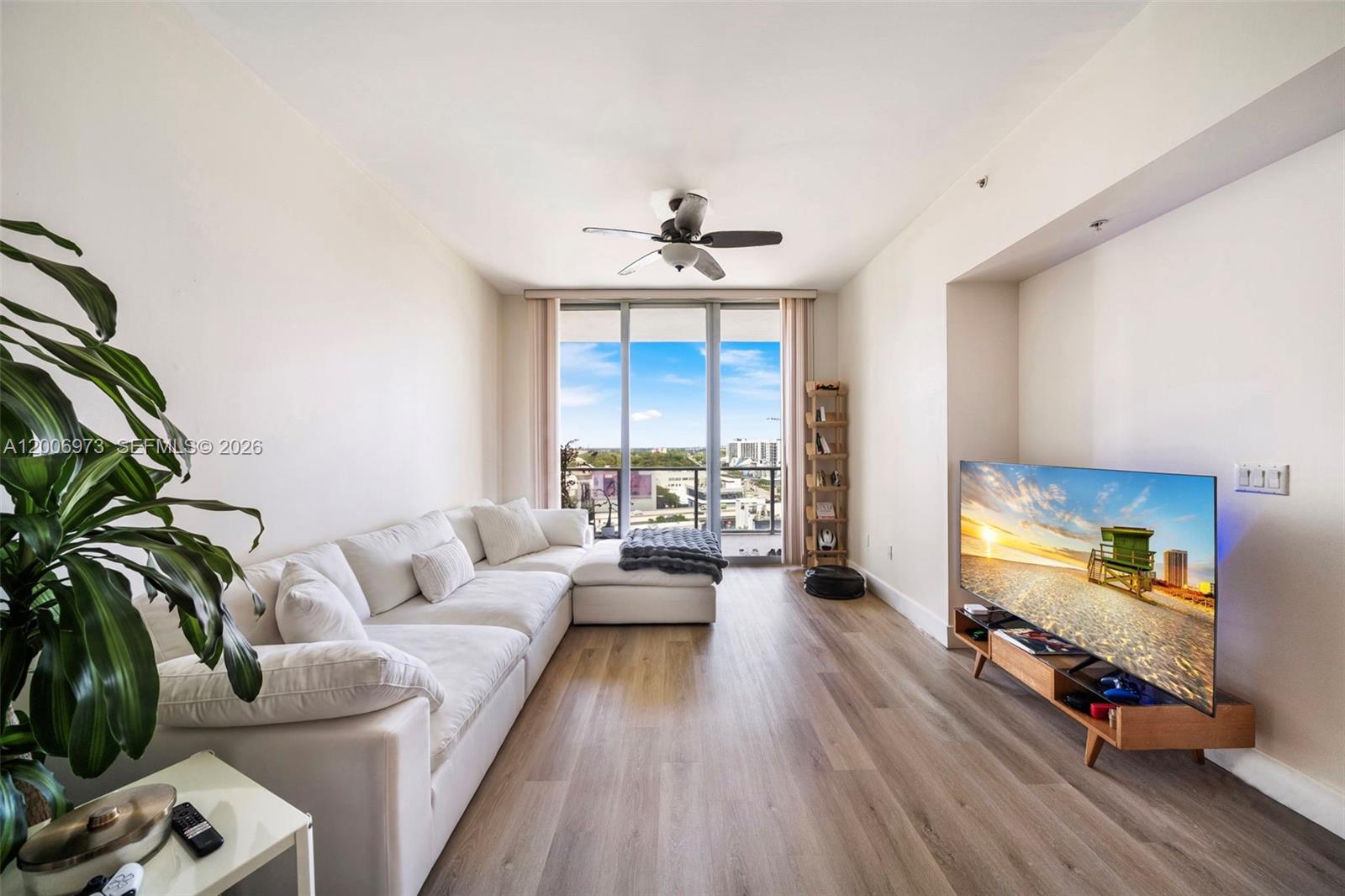 A living room features a white sectional sofa, a television on a stand, and balcony access — 3470 E Coast Ave # H1203, Miami FL 33137, MIAMI, FL