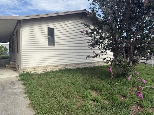 A side view of a light-colored mobile home with a carport and a flowering tree — 36118 ZINNIA AVENUE, ZEPHYRHILLS, FL