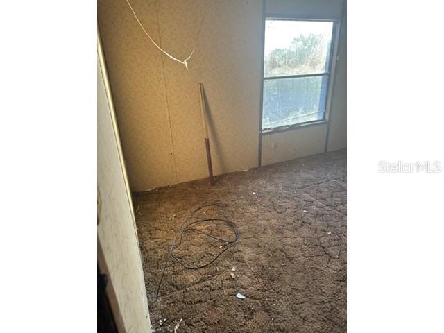 An empty room with brown carpet, wood-paneled walls, a window, and exposed electrical wiring — 36118 ZINNIA AVENUE, ZEPHYRHILLS, FL