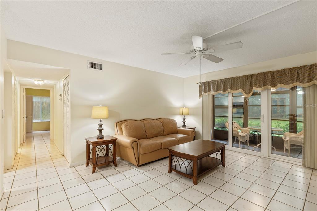 A living room features a tan leather sofa, a coffee table, and white tile flooring — 3232 LAKE PINE WAY E UNIT B1, TARPON SPRINGS, FL