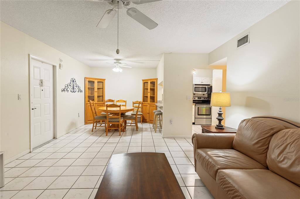 A living and dining area with white tile floors, a tan sofa, and wooden furniture — 3232 LAKE PINE WAY E UNIT B1, TARPON SPRINGS, FL
