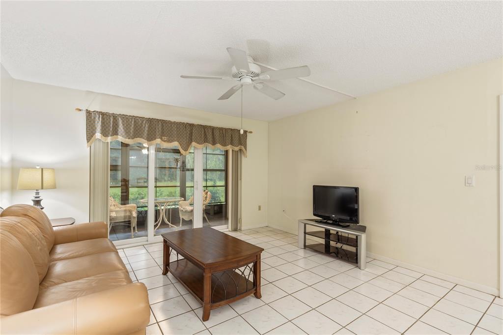 A living room with a tan leather sofa, coffee table, television, and sliding glass doors — 3232 LAKE PINE WAY E UNIT B1, TARPON SPRINGS, FL