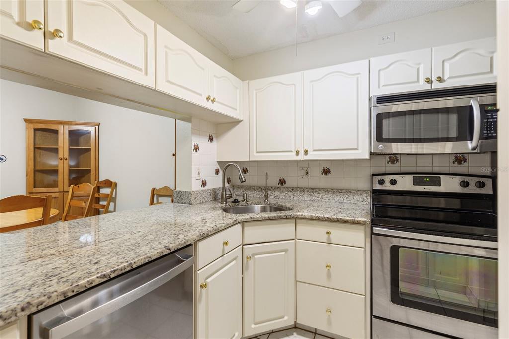 A kitchen with white cabinets, granite countertops, stainless steel appliances, and a pass-through window — 3232 LAKE PINE WAY E UNIT B1, TARPON SPRINGS, FL
