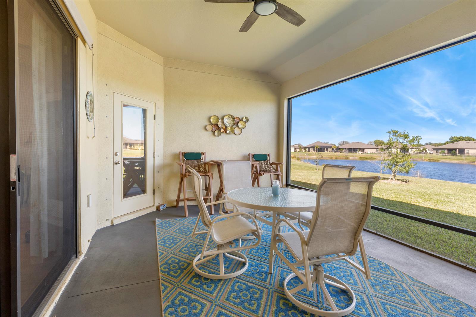 A screened-in patio features a dining set, a patterned rug, and views of a lake — 80 56th Court, Vero Beach FL 32968, VERO BEACH, FL