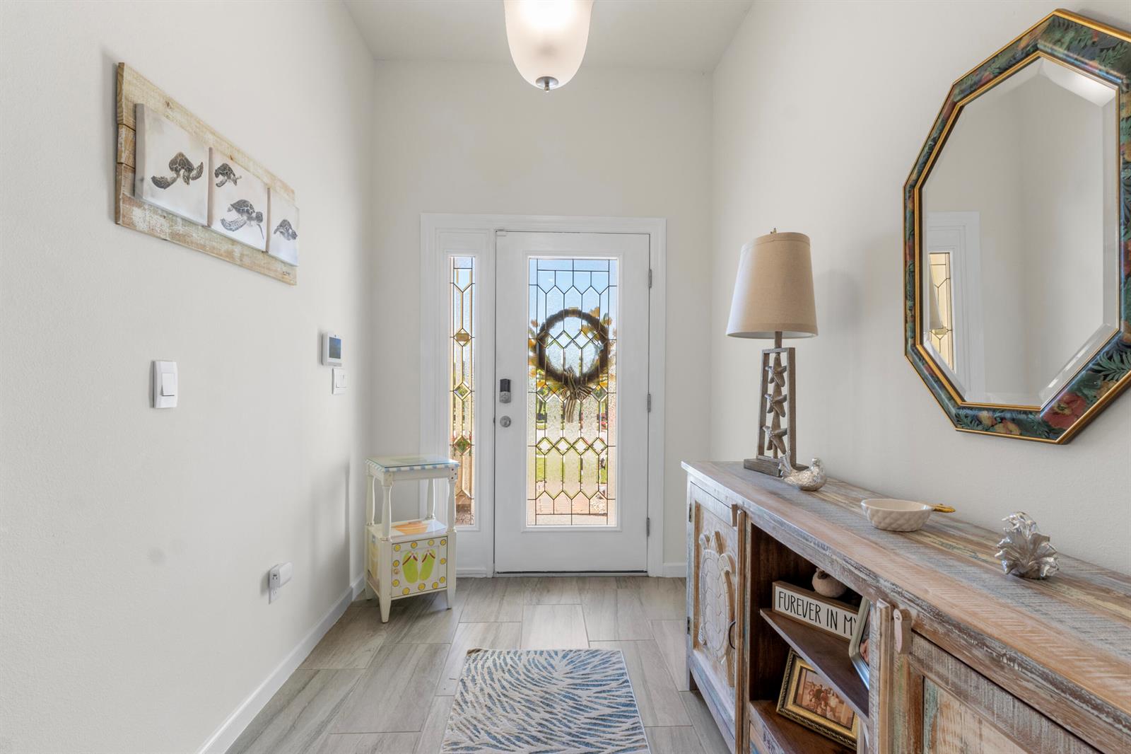 A bright entryway features a white front door, wood-look tile flooring, and coastal-themed decor — 80 56th Court, Vero Beach FL 32968, VERO BEACH, FL