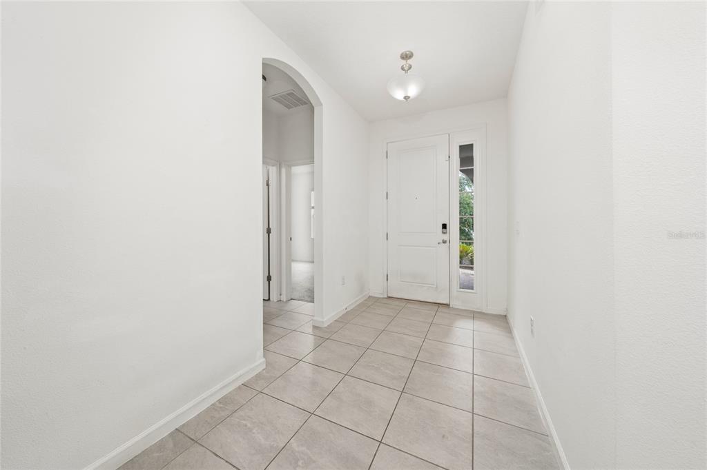 An entryway with white walls, light-colored tile flooring, an arched doorway, and a front door — 417 SAPPHIRE DRIVE, DAVENPORT, FL