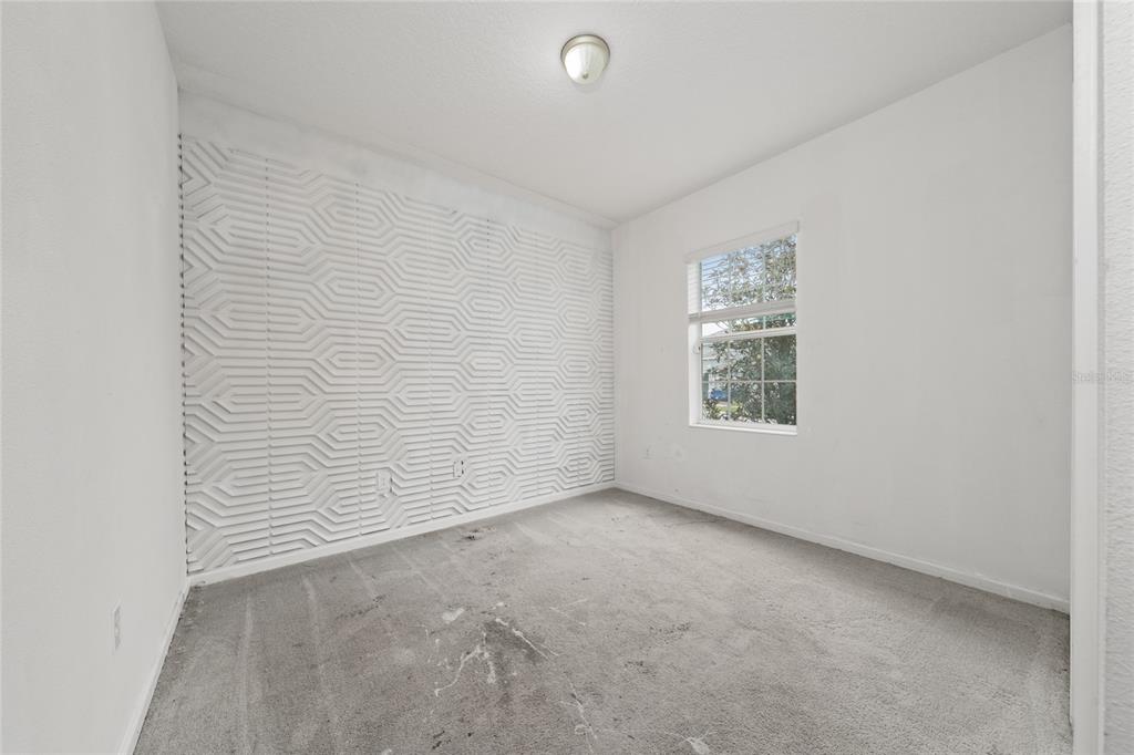 A bedroom with gray carpet, white walls, a textured accent wall, and a single window — 417 SAPPHIRE DRIVE, DAVENPORT, FL