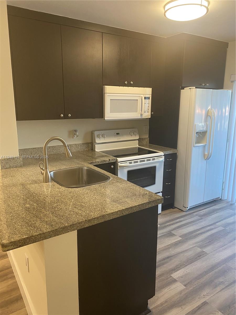 A kitchen features dark cabinets, granite countertops, white appliances, and wood-look flooring — 2575 SW 27th Ave # 212, Coconut Grove FL 33133, COCONUT GROVE, FL