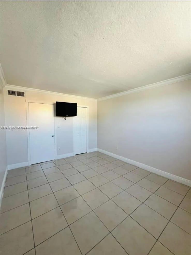An empty room features light-colored tile flooring, white walls, crown molding, and two closed doors — 606 W 81st St # 224, Hialeah FL 33014, HIALEAH, FL