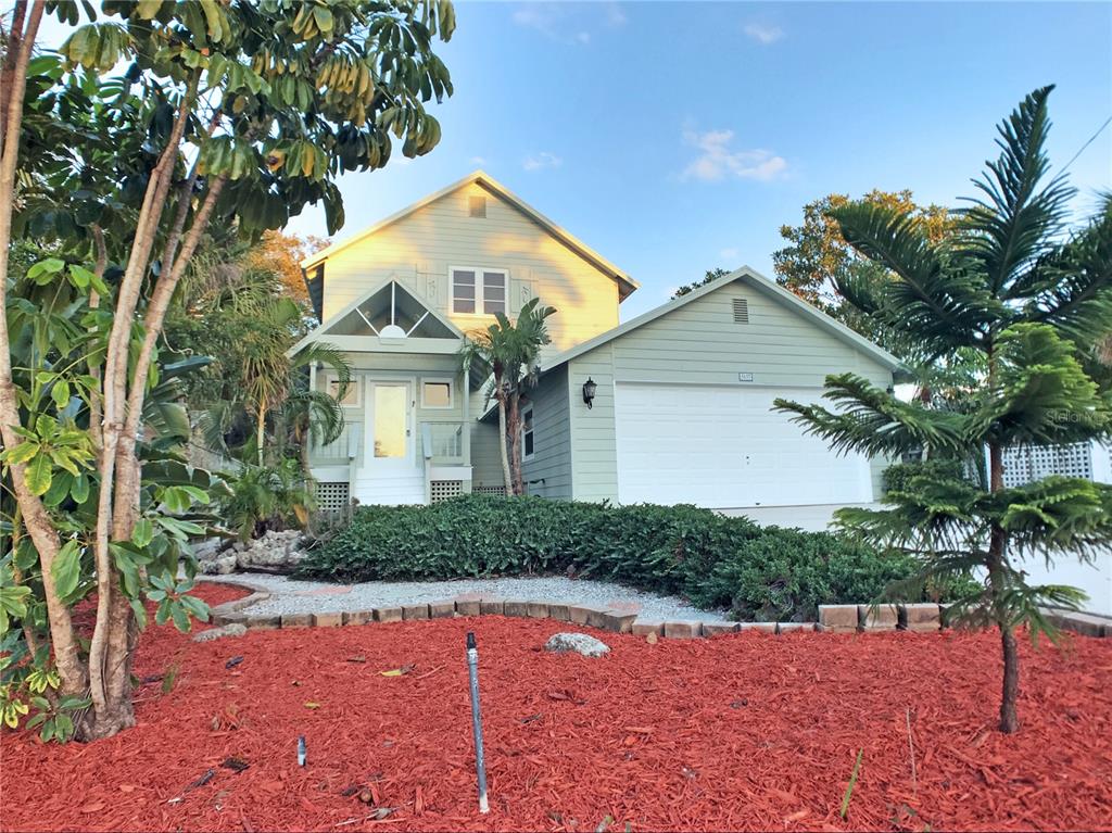 A two-story light green house with a front porch, garage, and landscaped yard — 5157 SANDY BEACH AVENUE, SARASOTA, FL